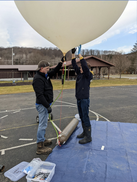 Two individuals attach CubeSat Emulator materials to a High Altitude Balloon.